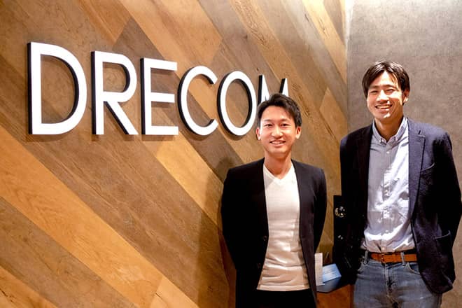 Picture of two men in business casual attire with company name Drecom in the background